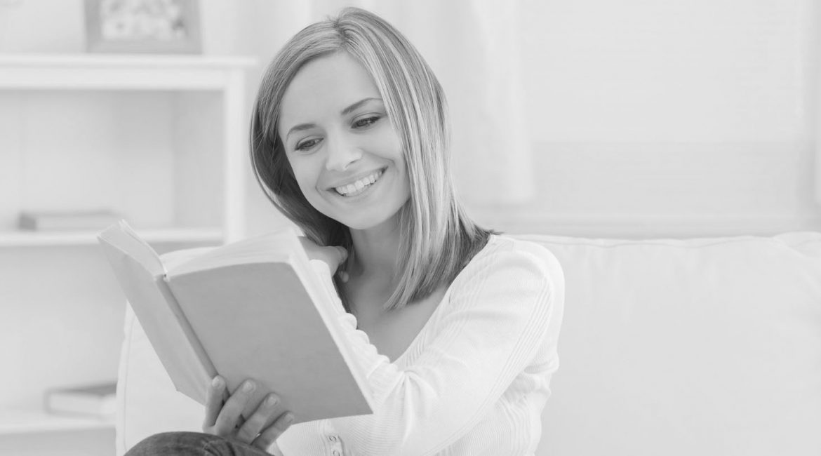 Happy young woman reading storybook on couch at home